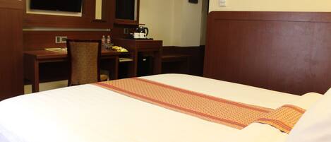 A hotel room with a large bed, a desk, a chair, a television, and a coffee maker.
