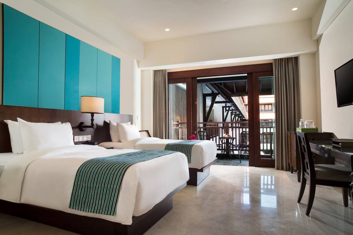 A hotel room with two beds, a desk, and a view of a balcony.