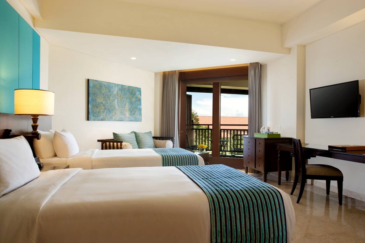 A hotel room with two beds, a desk, a chair, a television, and a balcony with a view.