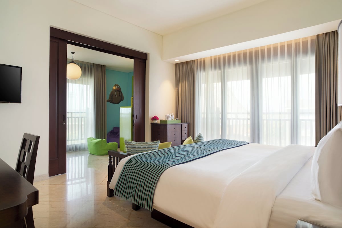 A hotel room with a large bed, a desk, a chair, a television, and a view of the outside through the window.