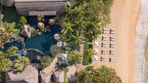 An aerial view of a resort with a swimming pool, palm trees, and beach chairs.