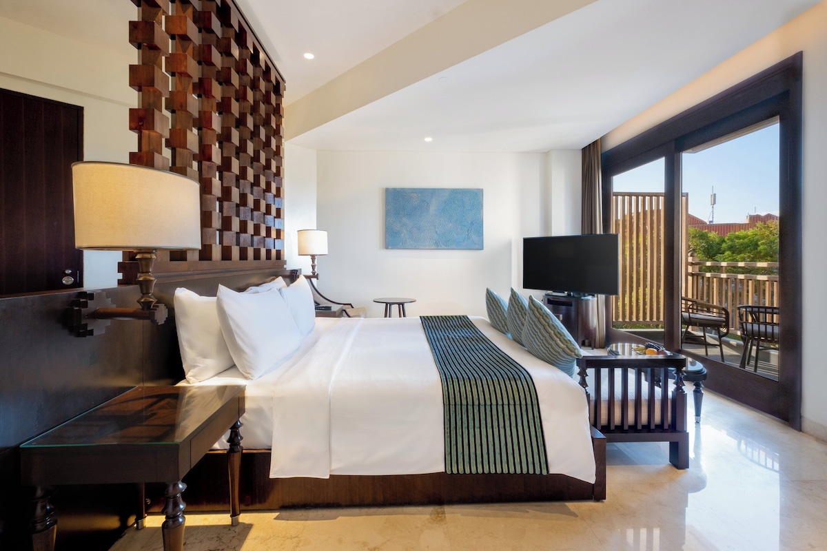 A modern hotel room with a large bed, a TV, a desk, and a balcony with a view.