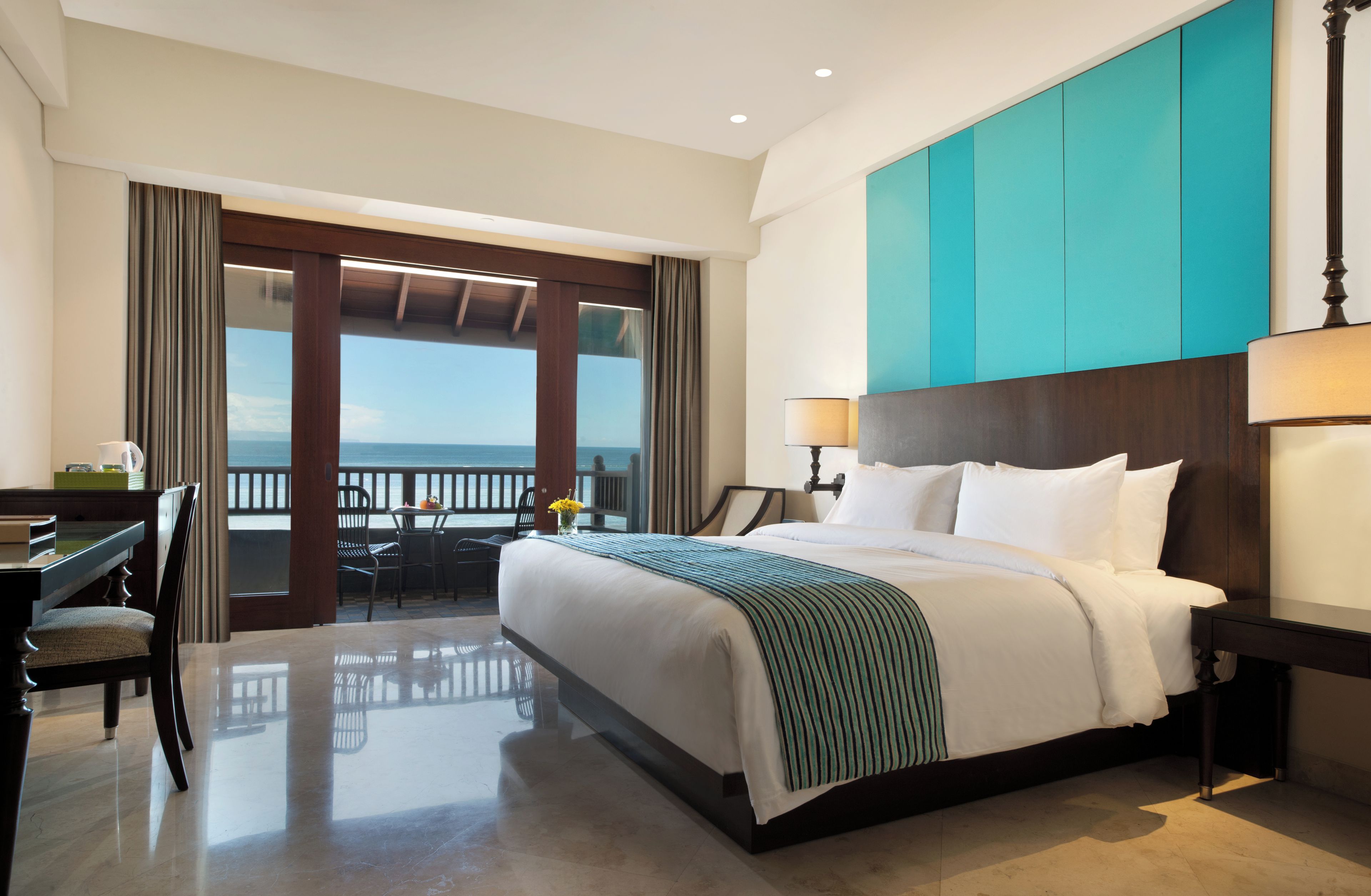 Une chambre d’hôtel avec un lit, un bureau, une chaise, une lampe et une vue sur la mer.