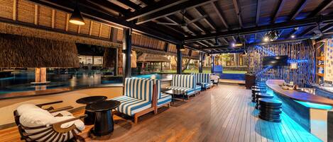 A wooden deck with striped seating, a bar area, and a thatched-roof structure.