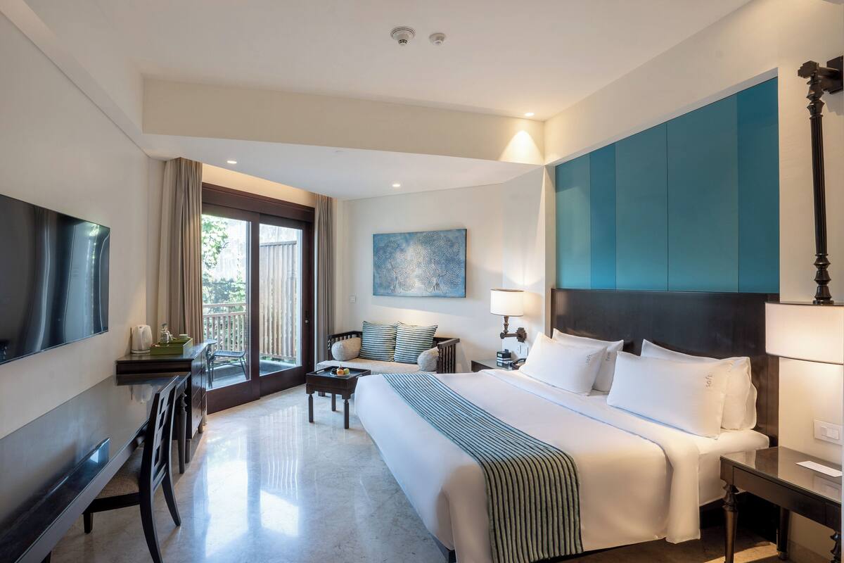 A hotel room with a large bed, a desk, a chair, a TV, and a window with curtains.