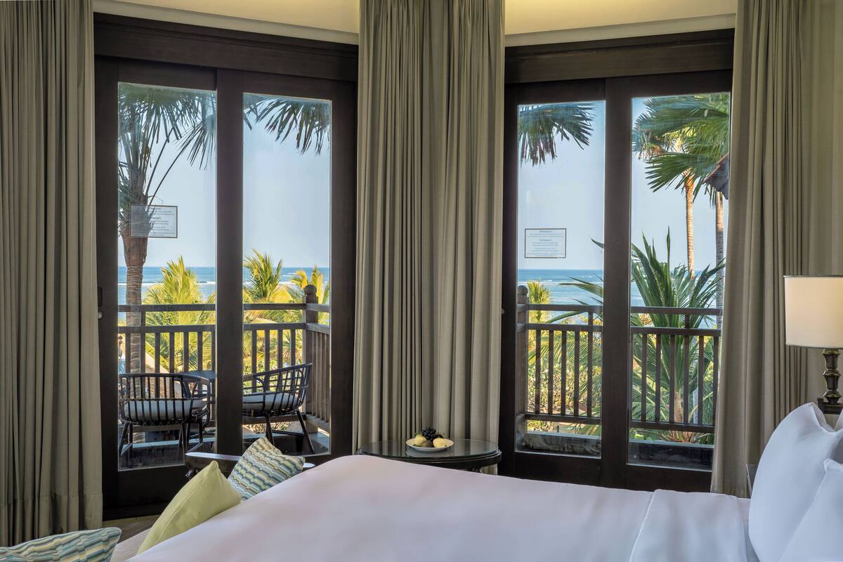 A hotel room with a balcony, a bed, a small table with a plate of fruit, and a chair.