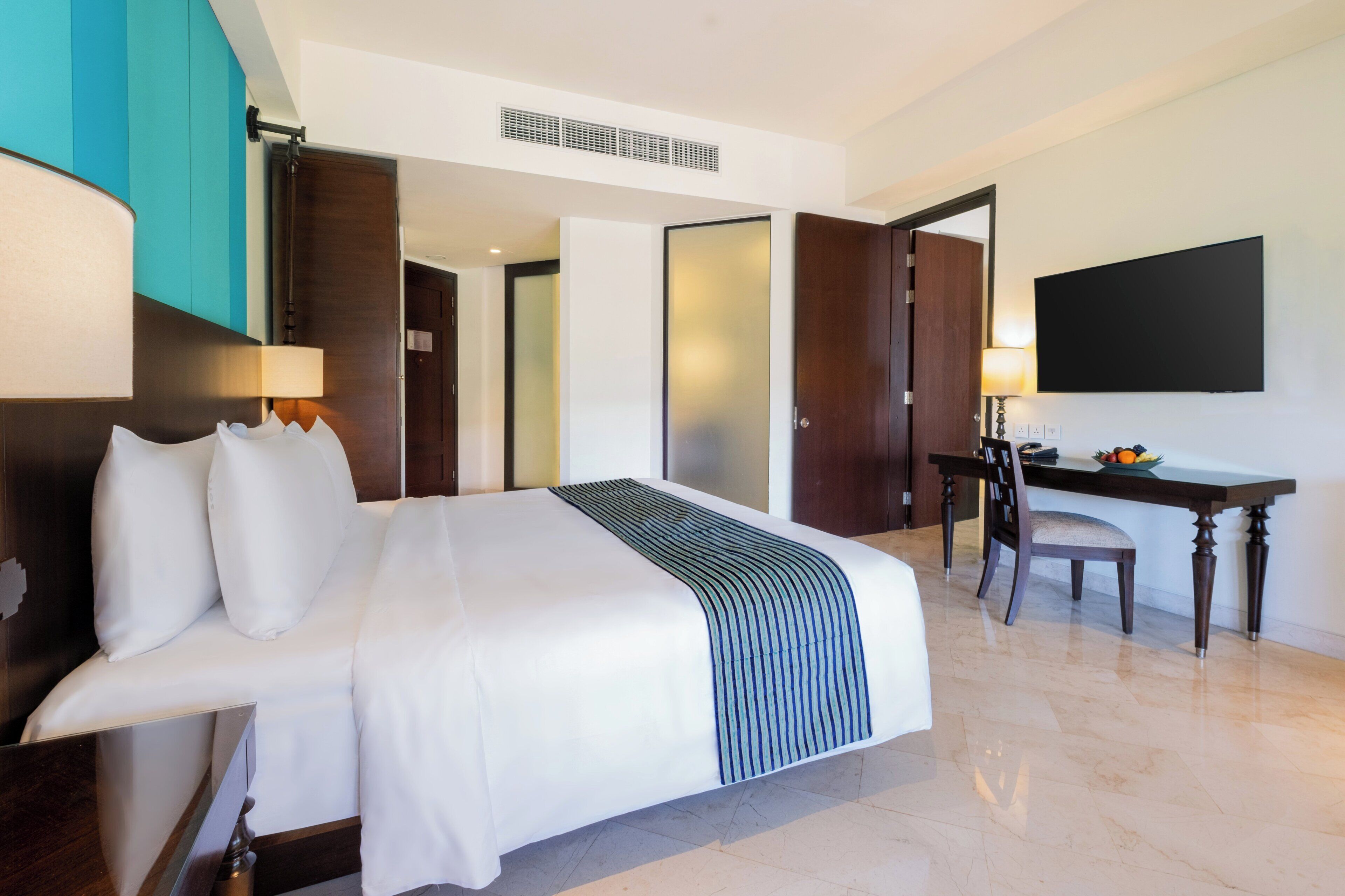 Hotelkamer met een groot bed, een bureau, een stoel, een flatscreen televisie en een deur naar een andere kamer.