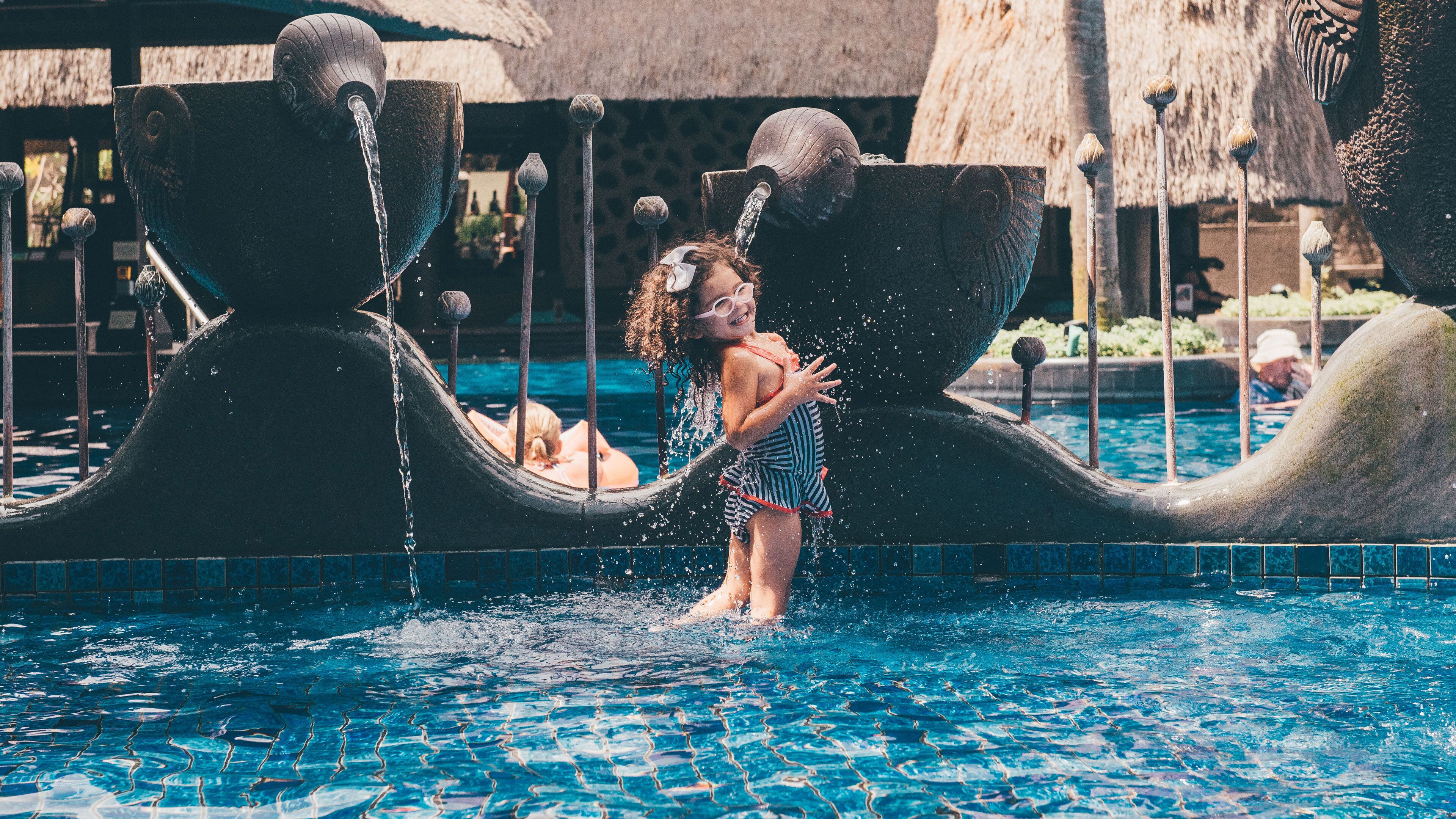 Niño jugando en una fuente con una gran escultura abstracta.