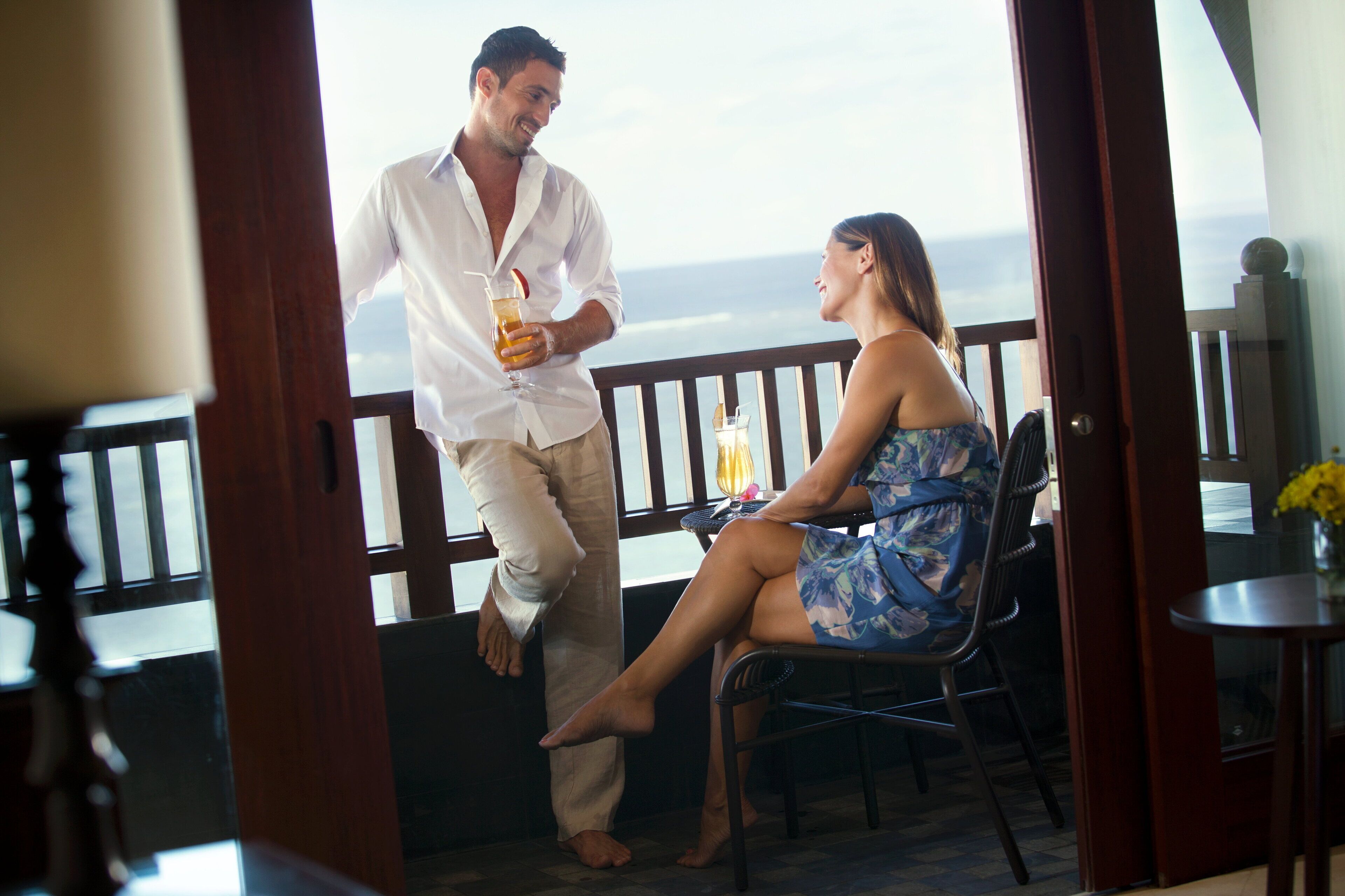 A man and woman sitting on a balcony with a view of the ocean.