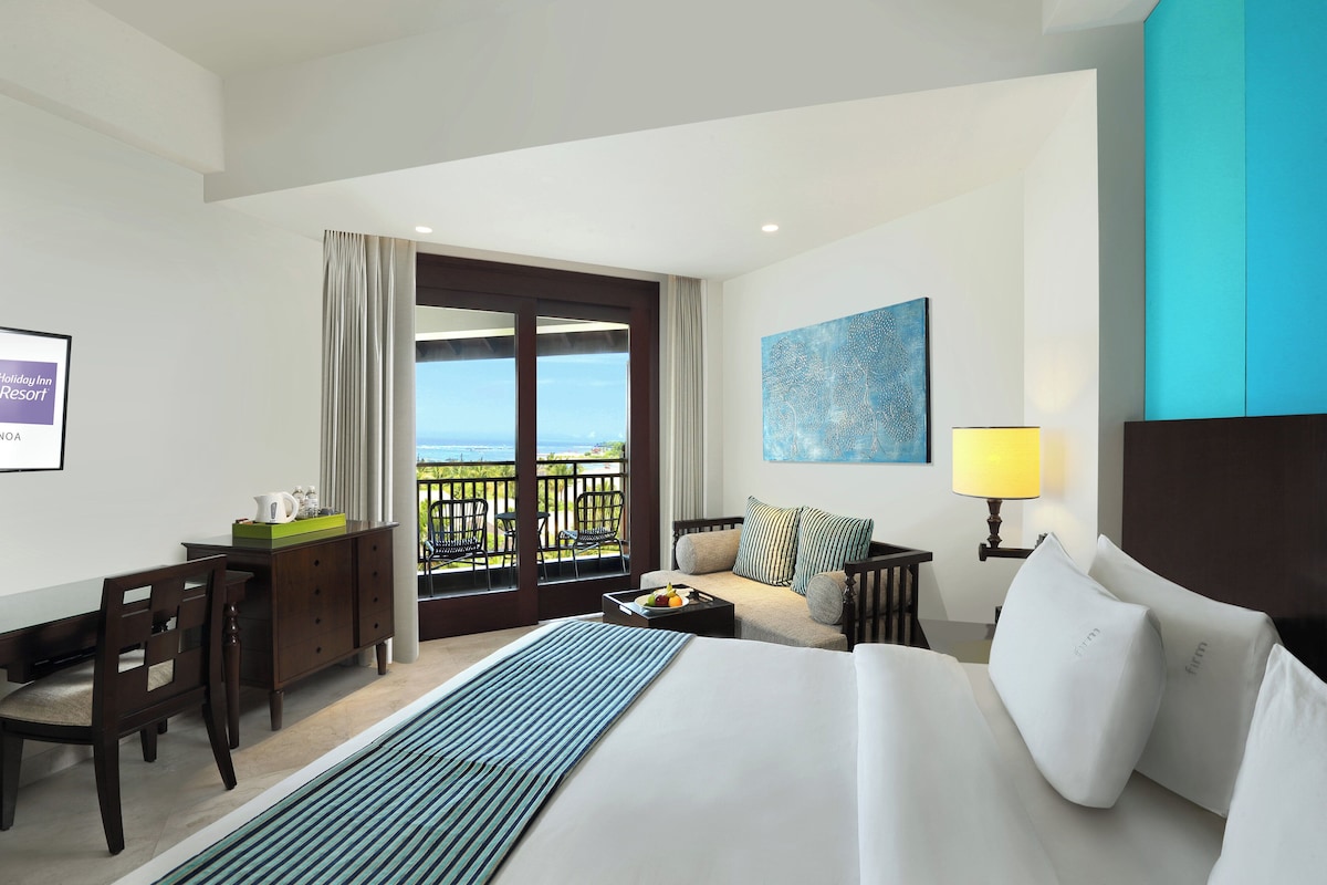 A hotel room with a large bed, a sofa, a desk, and a view of the ocean.