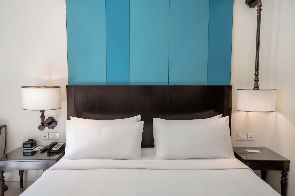 A hotel room with a large bed, two bedside tables, a nightstand, a lamp, a telephone, and a wall panel.