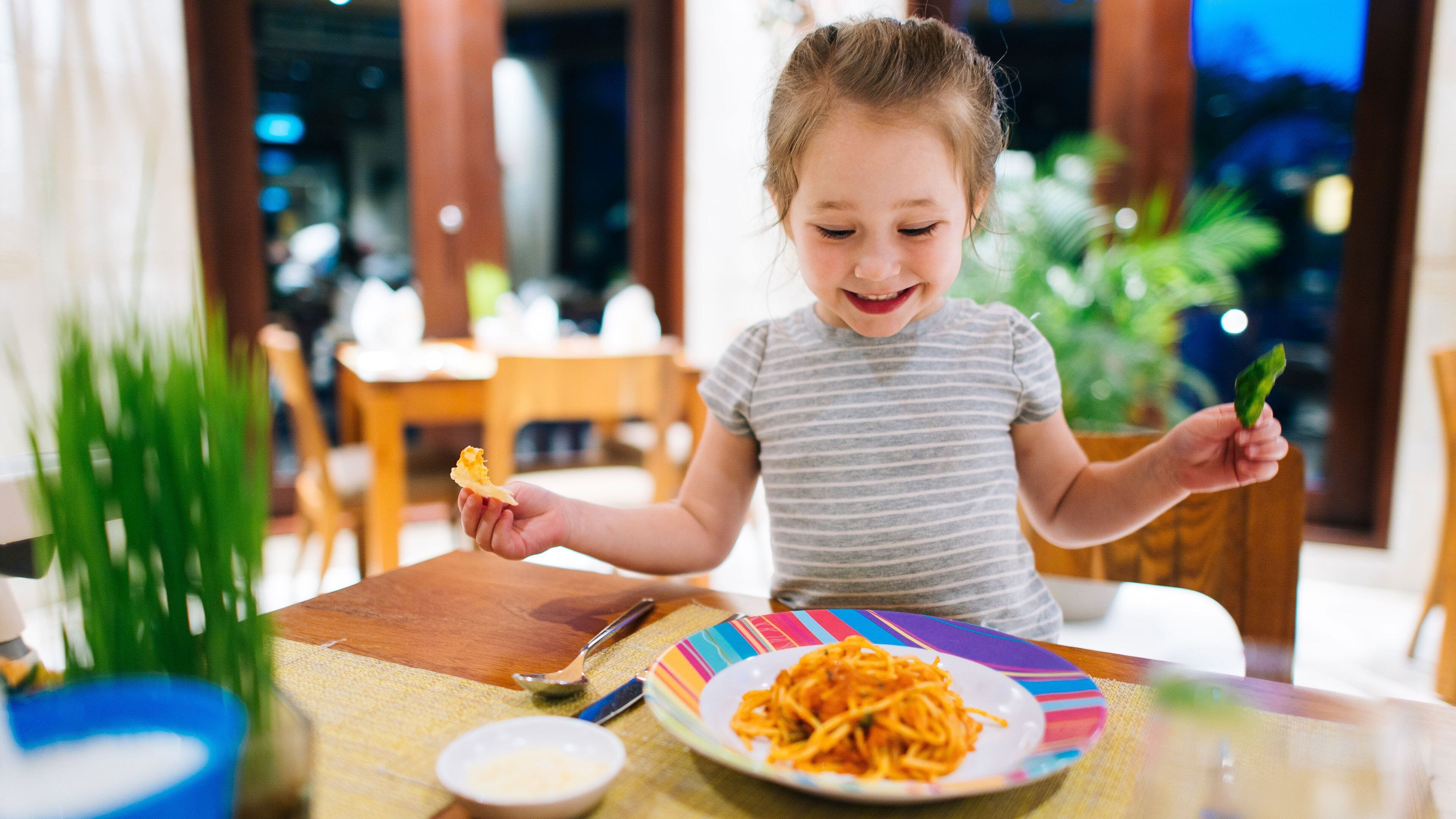 A child sitting at a table with a plate of spaghetti and a small bowl of sauce.