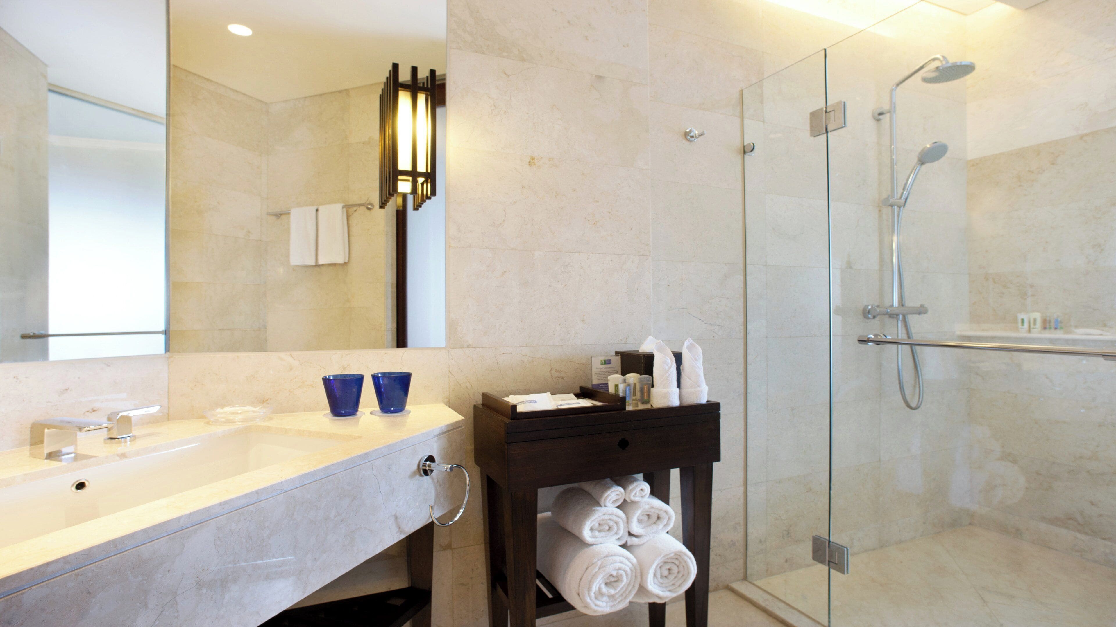 A modern bathroom with a glass shower enclosure, a marble sink, and a towel rack.