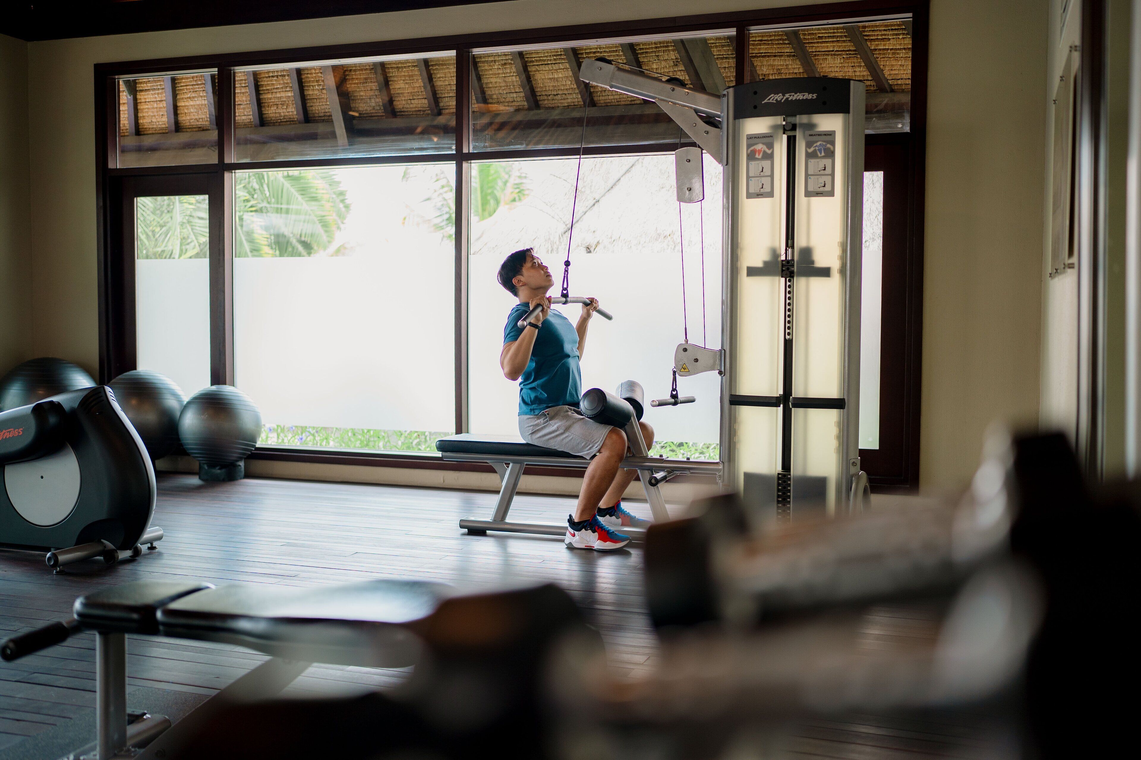 A gym with exercise equipment, large windows, and a view of greenery outside.