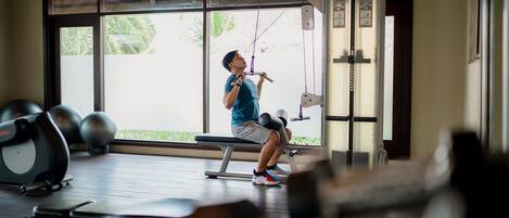 A gym with exercise equipment, large windows, and a view of greenery outside.
