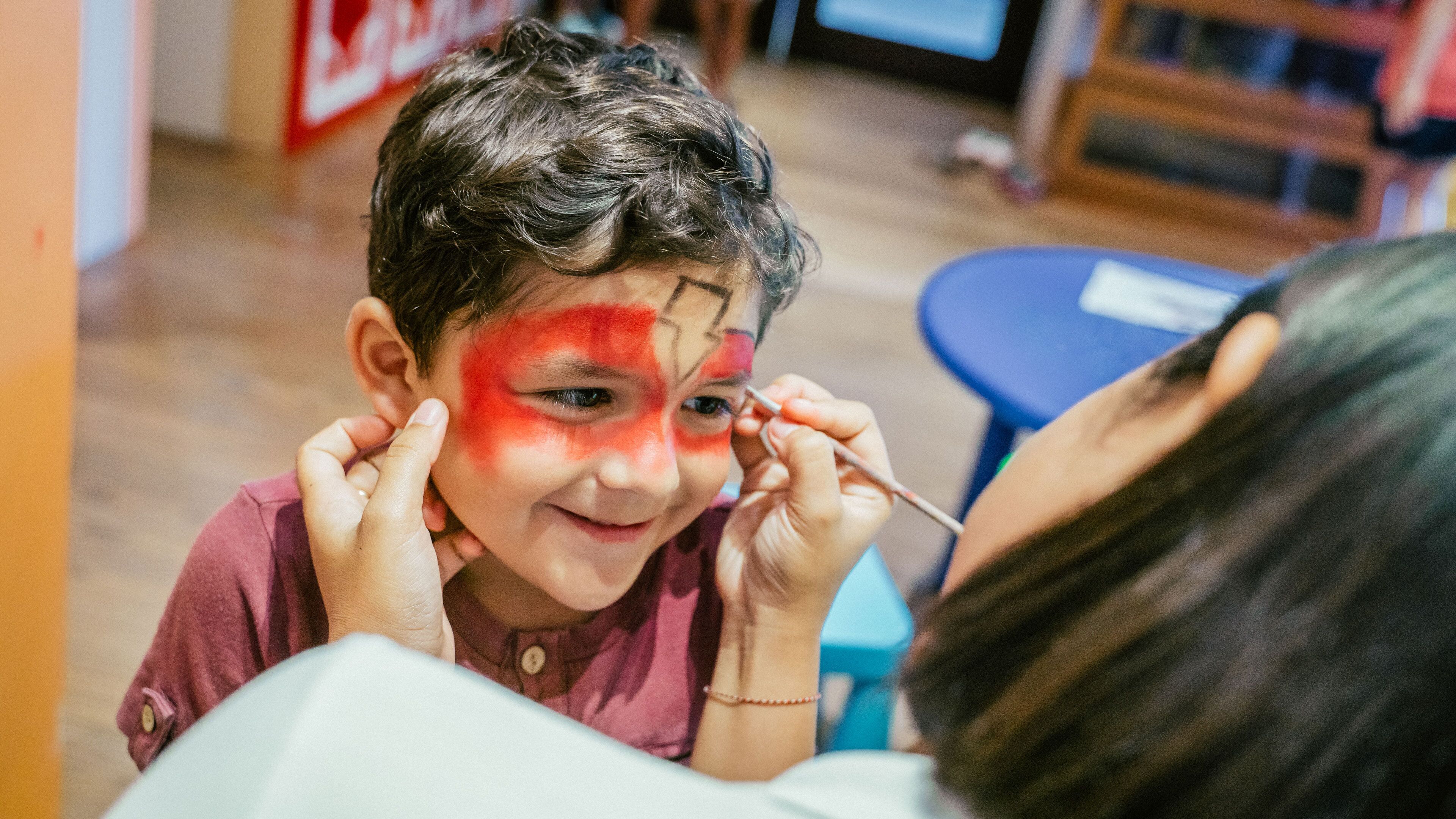 A child with red paint on their face, being attended to by an adult.