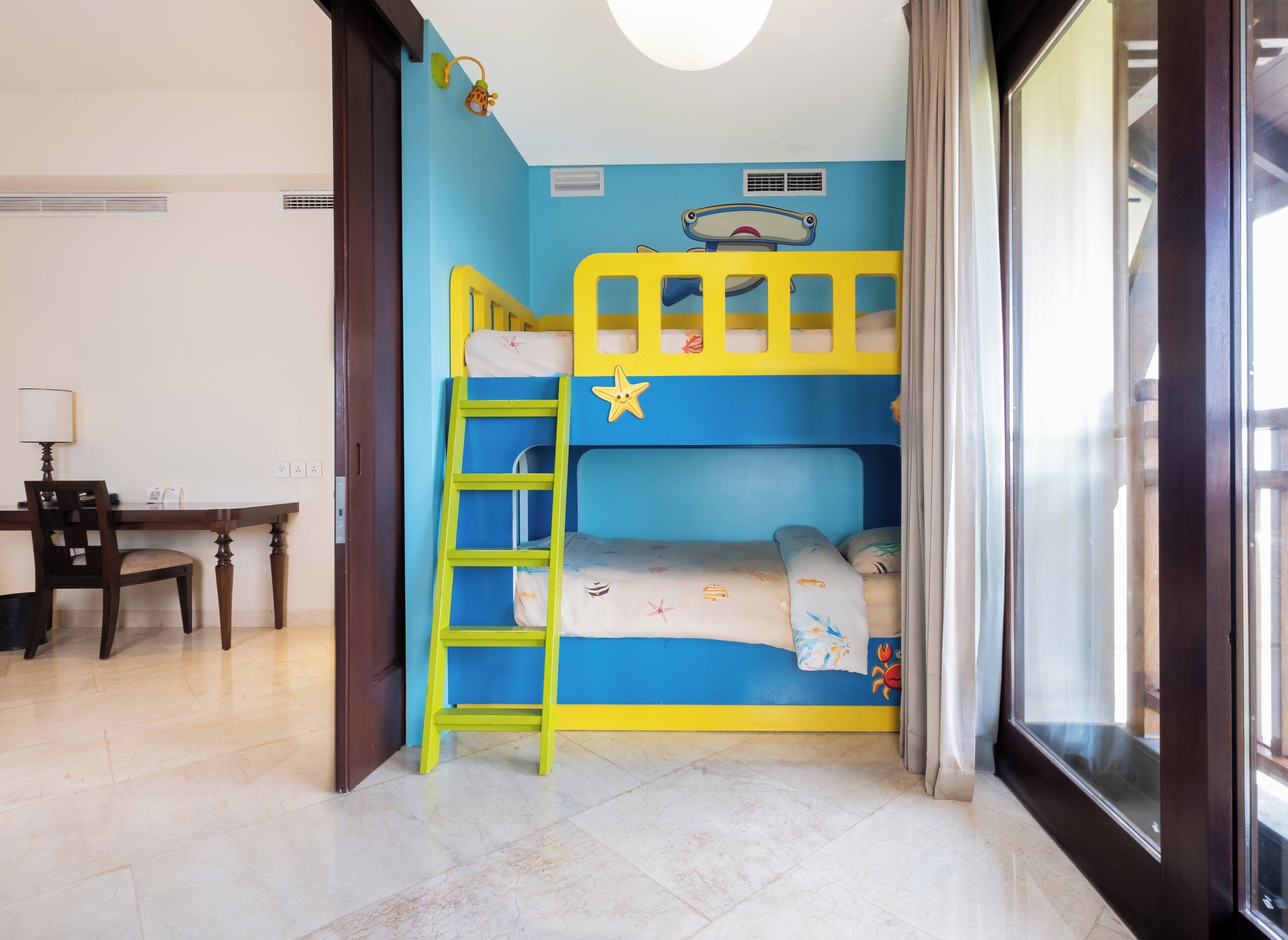 Una cama litera con escalera, un escritorio con silla y una ventana con cortinas.