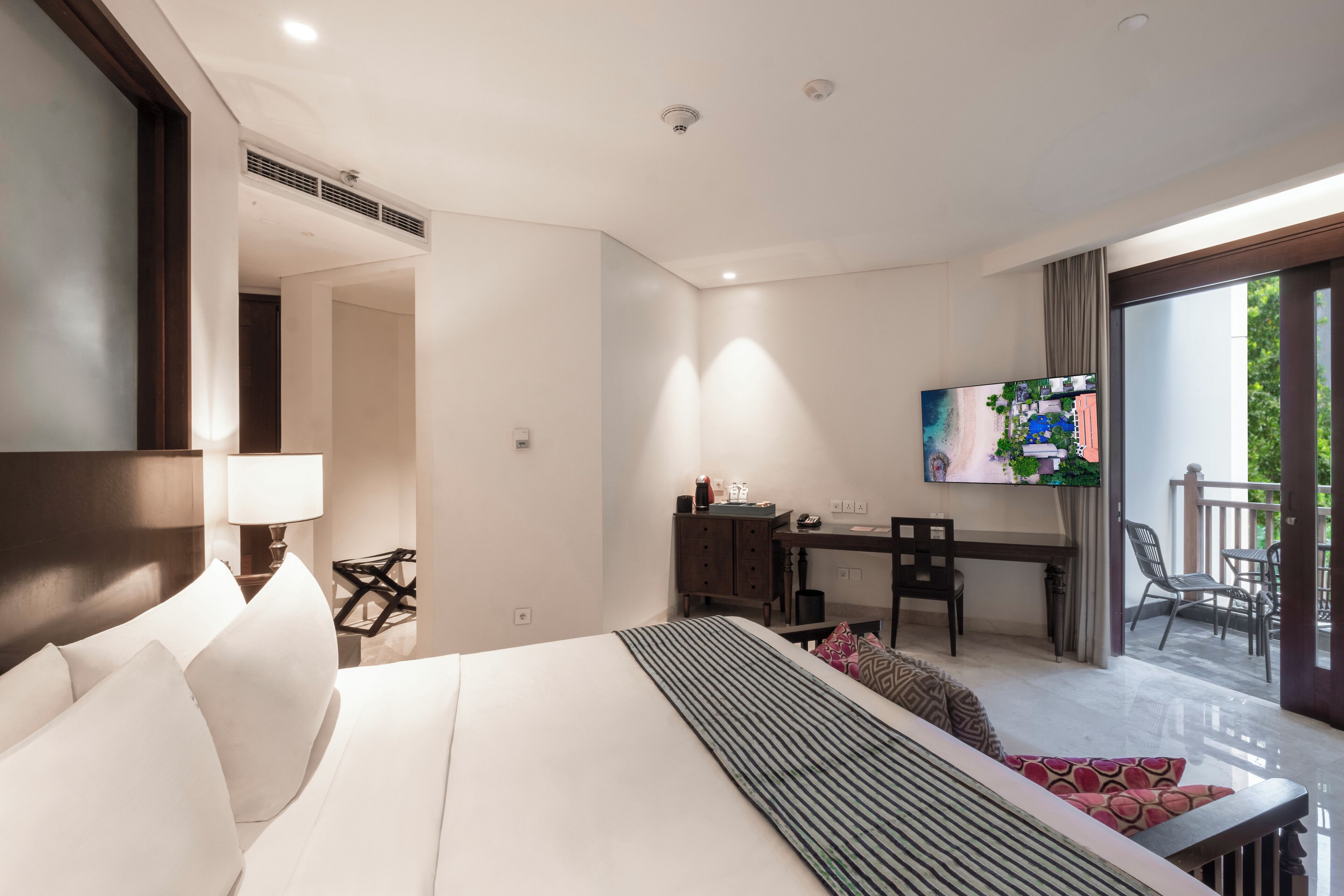 A hotel room with a large bed, a desk, a chair, a TV, and a balcony.