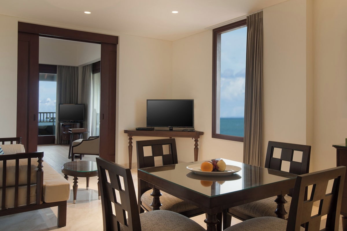 A hotel room with a dining table, chairs, a television, and a view of the ocean.