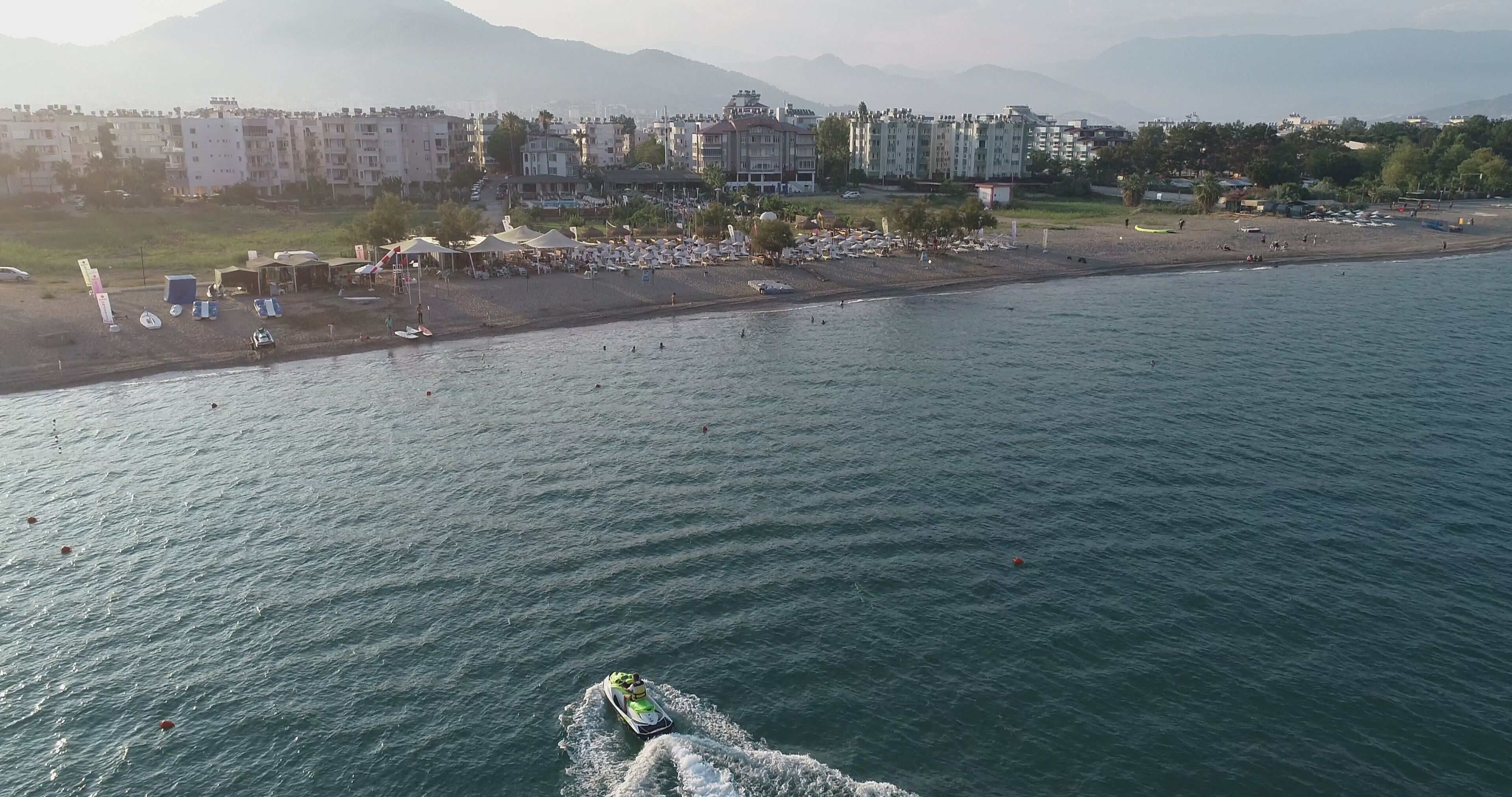 Zona costera con playa, edificios y un jet ski en el agua.
