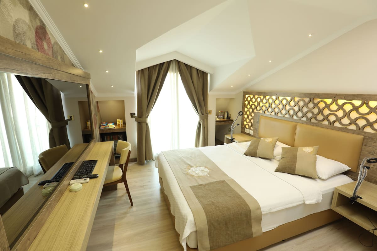 Quarto de hotel com uma cama grande, uma escrivaninha com computador e um espaço de estar.