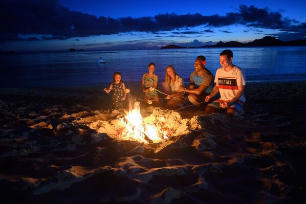 A group of people sitting around a campfire on a beach at dusk. - Sheraton Resort & Spa, Tokoriki Island, Fiji (Tokoriki Island)