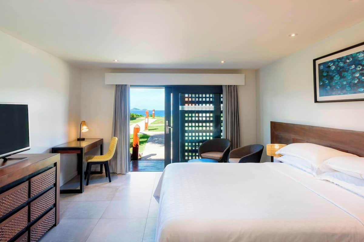A hotel room with a bed, a desk, a chair, a TV, and a view of the outdoors.
