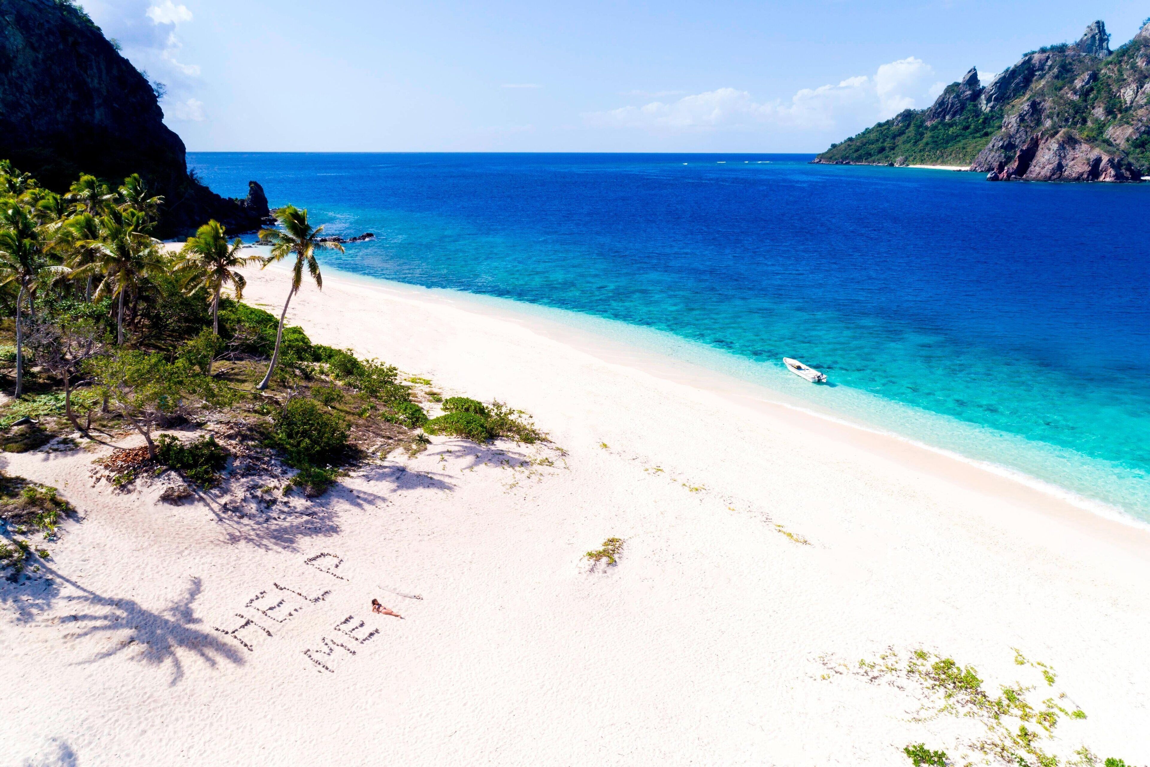 A beach with clear turquoise water, white sand, and palm trees.