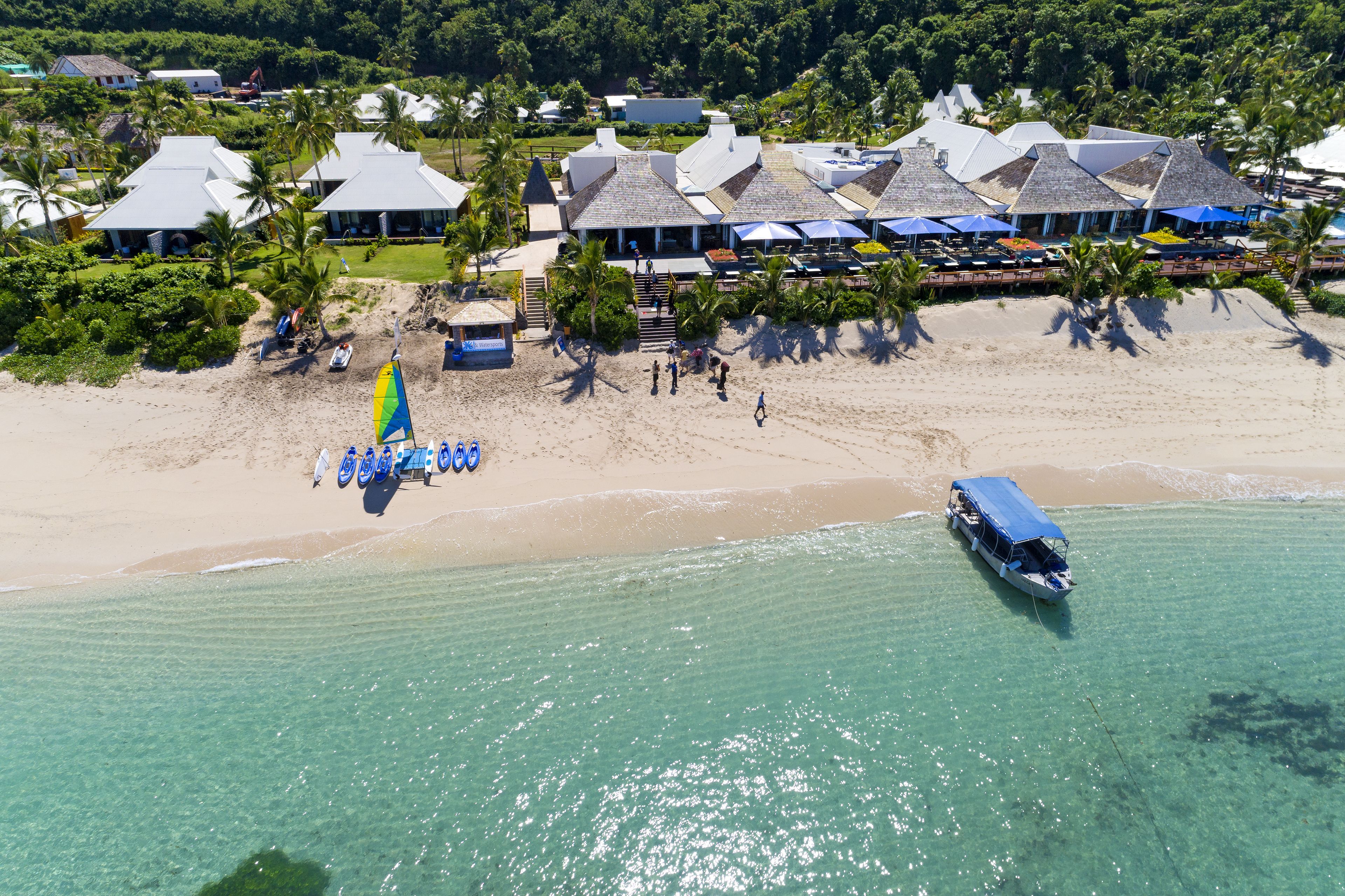 A beachside resort with multiple bungalow-style buildings, a clear turquoise sea, and a boat docked near the shore.