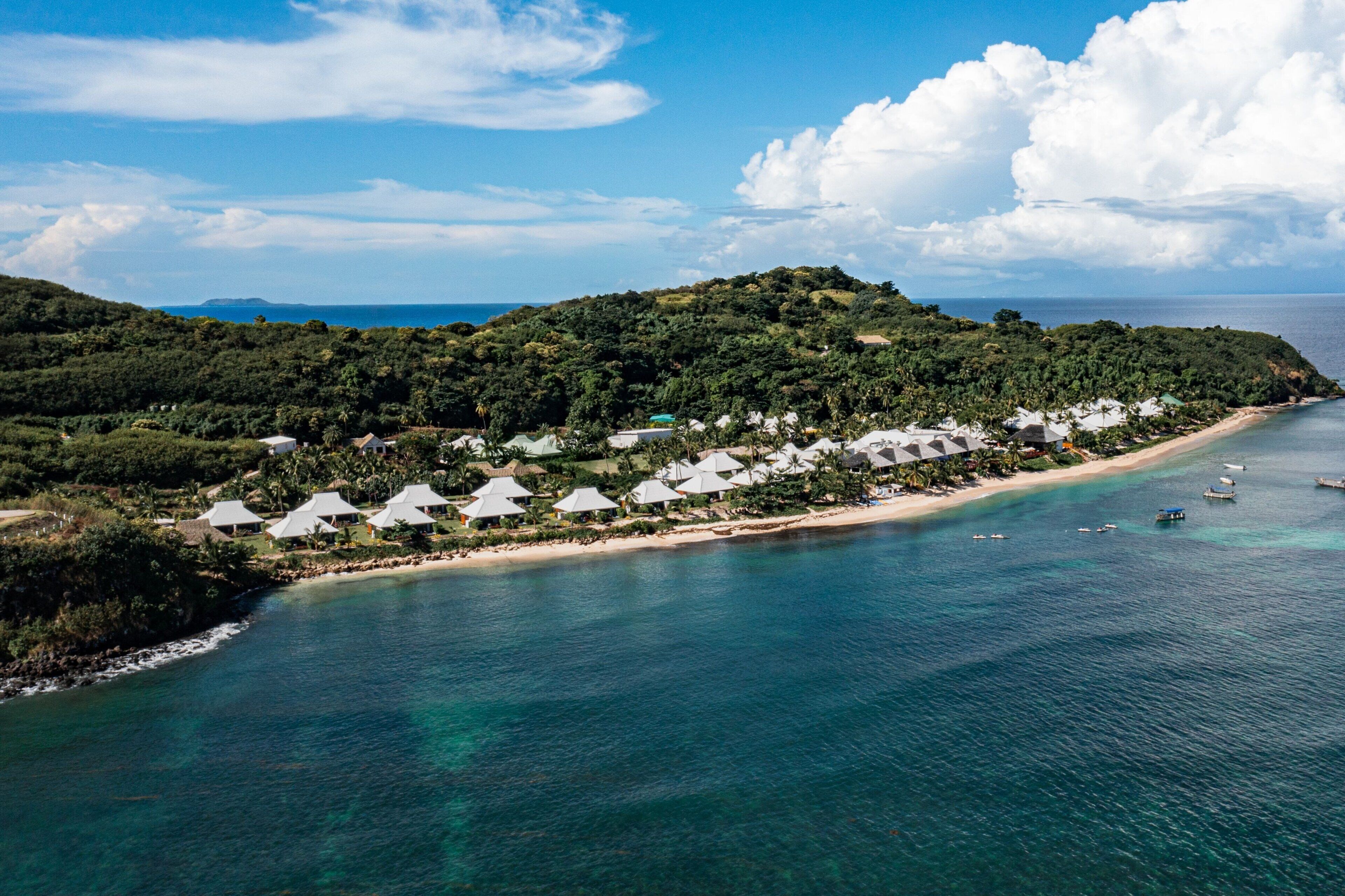 An aerial view of a coastal resort with beach huts, a sandy beach, and clear blue waters.