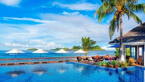 A pool area with lounge chairs and umbrellas, a palm tree, and a view of the ocean. - Sheraton Resort & Spa, Tokoriki Island, Fiji (Tokoriki Island)