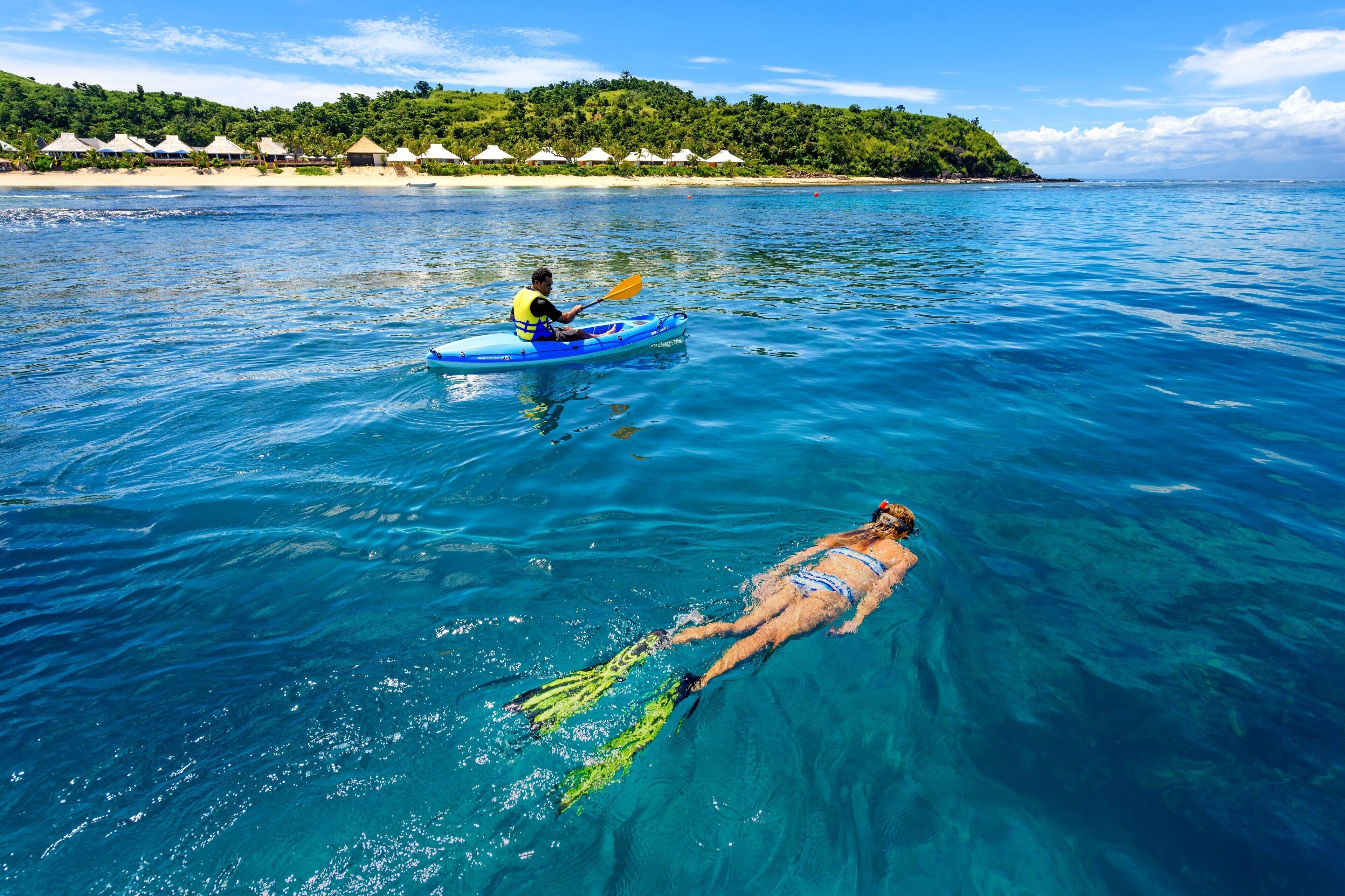 Une mer d’un bleu limpide, où l’on aperçoit une personne pratiquant le kayak et une autre nageant.