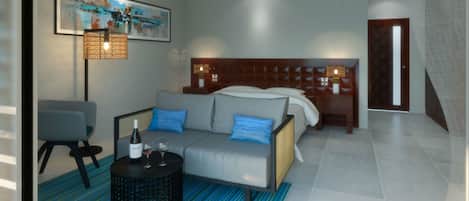 Une chambre d’hôtel moderne avec un lit, un canapé, une petite table avec une bouteille et des verres, une chaise et un tableau au mur.