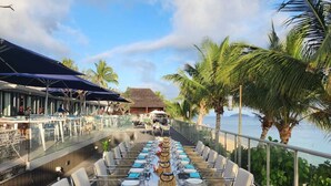 An outdoor dining area with a long table set for a meal, surrounded by chairs, with a view of the ocean and palm trees. - Sheraton Resort & Spa, Tokoriki Island, Fiji (Tokoriki Island)