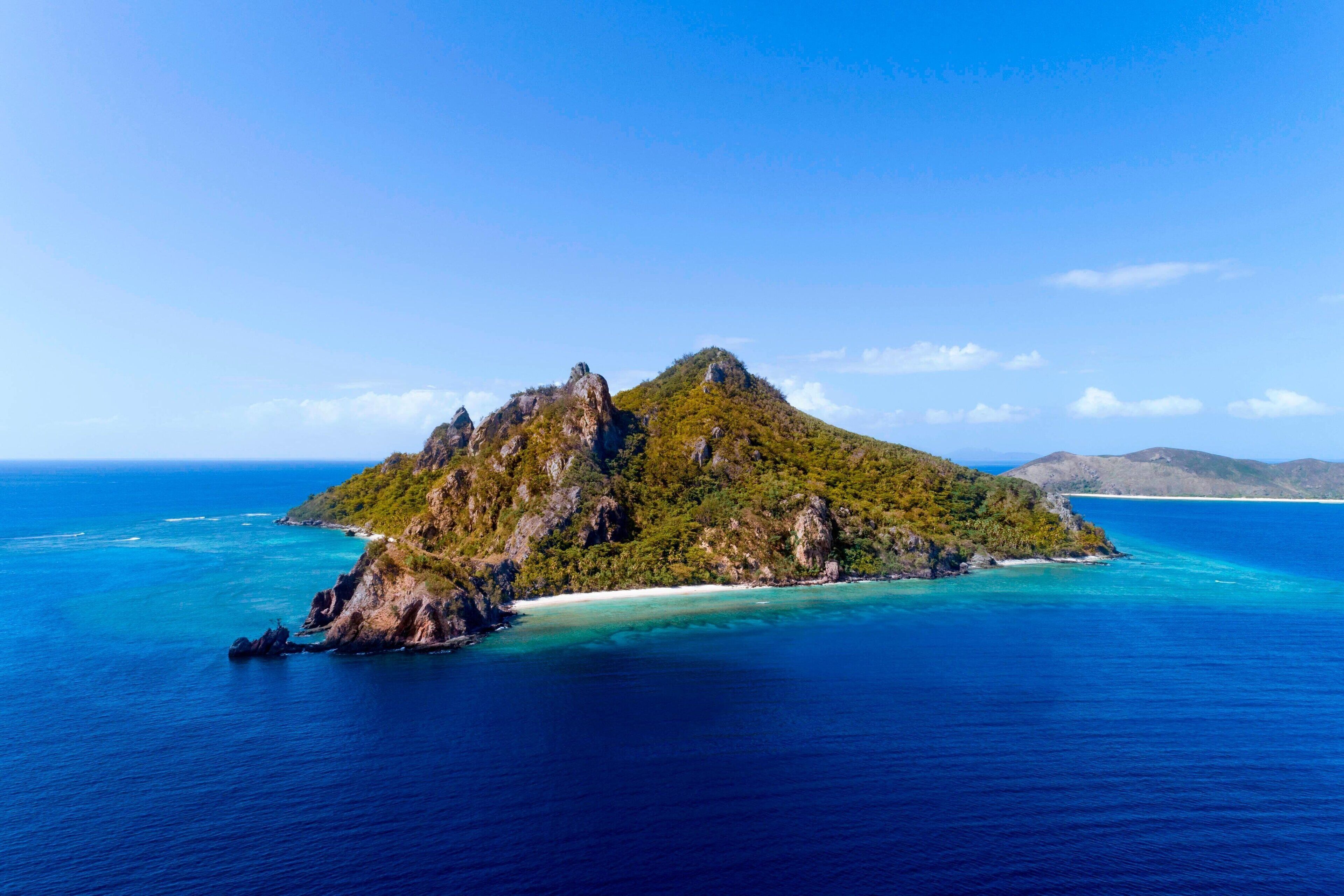 Eine tropische Insel mit markantem Gipfel, umgeben von klarem türkisblauem Wasser und wolkenlosem Himmel.