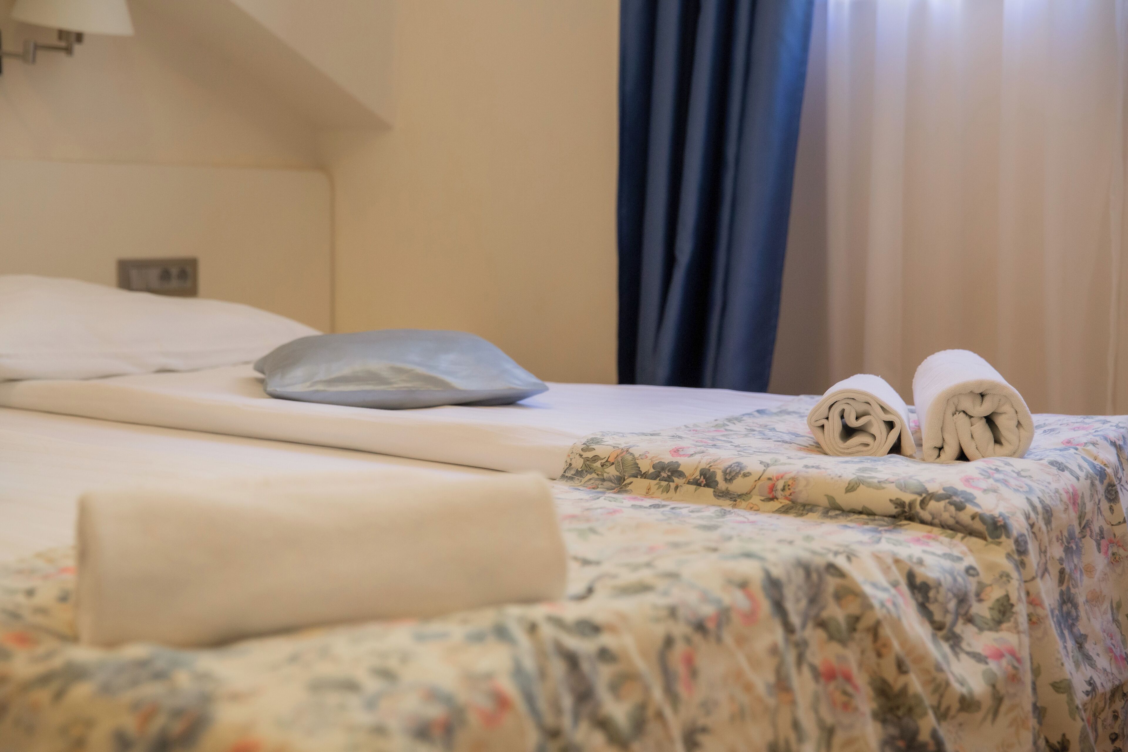 A neatly made bed with a floral bedspread, a pillow, and rolled towels.