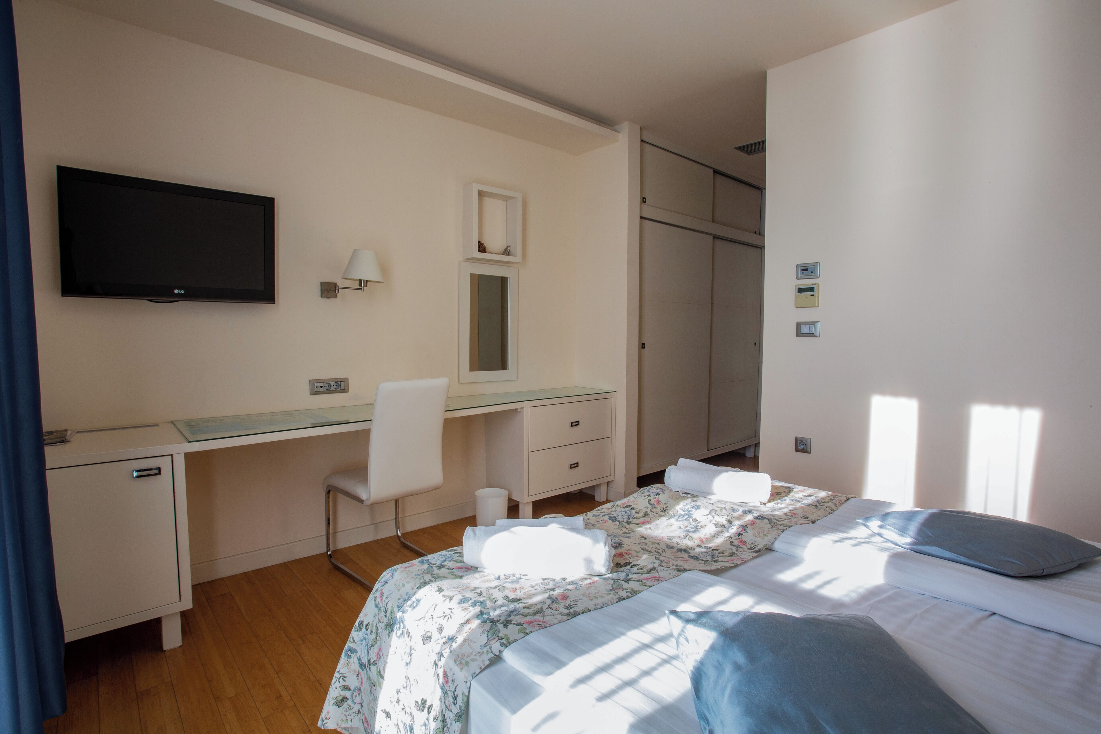 Une chambre d’hôtel comprenant un lit, un bureau avec une chaise, un téléviseur fixé au mur, un miroir et une armoire.
