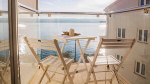Un balcon avec deux chaises en bois et une petite table, d’où l’on peut admirer un plan d’eau et des montagnes lointaines.