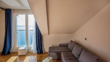 A modern living room with a sectional sofa, a glass coffee table, and a view of the sea through large windows.