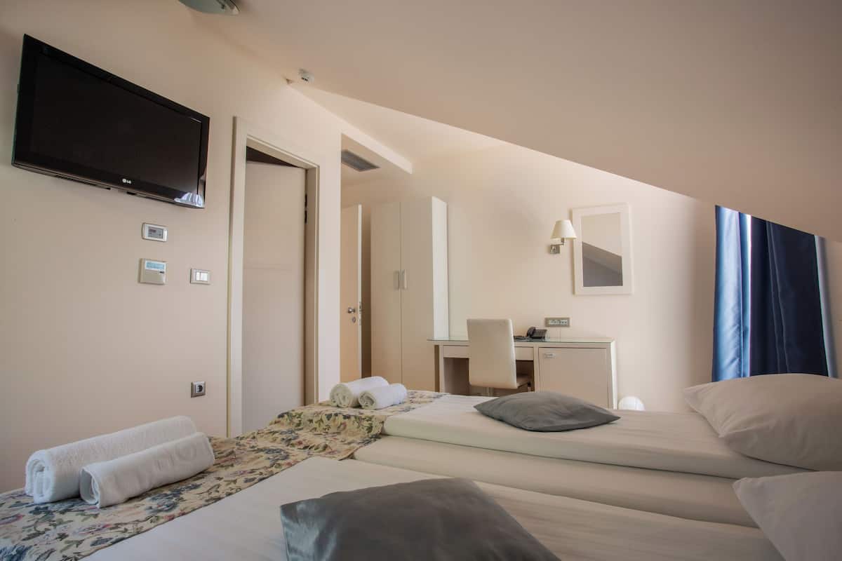 Habitación de hotel con dos camas, un escritorio, una silla, un televisor y un baño visible a través de una puerta abierta.