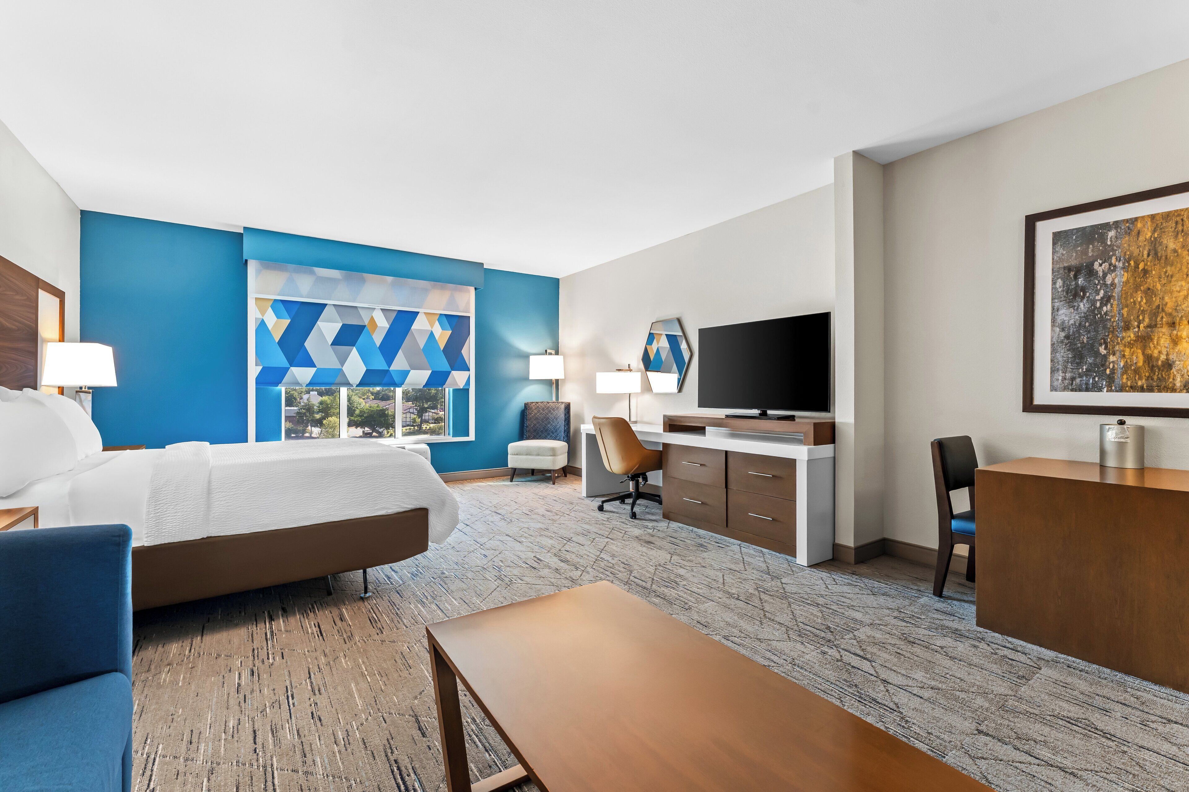 A hotel room with a bed, desk, chair, and a TV.