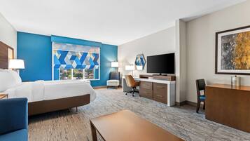 A hotel room with a bed, desk, chair, and a TV.