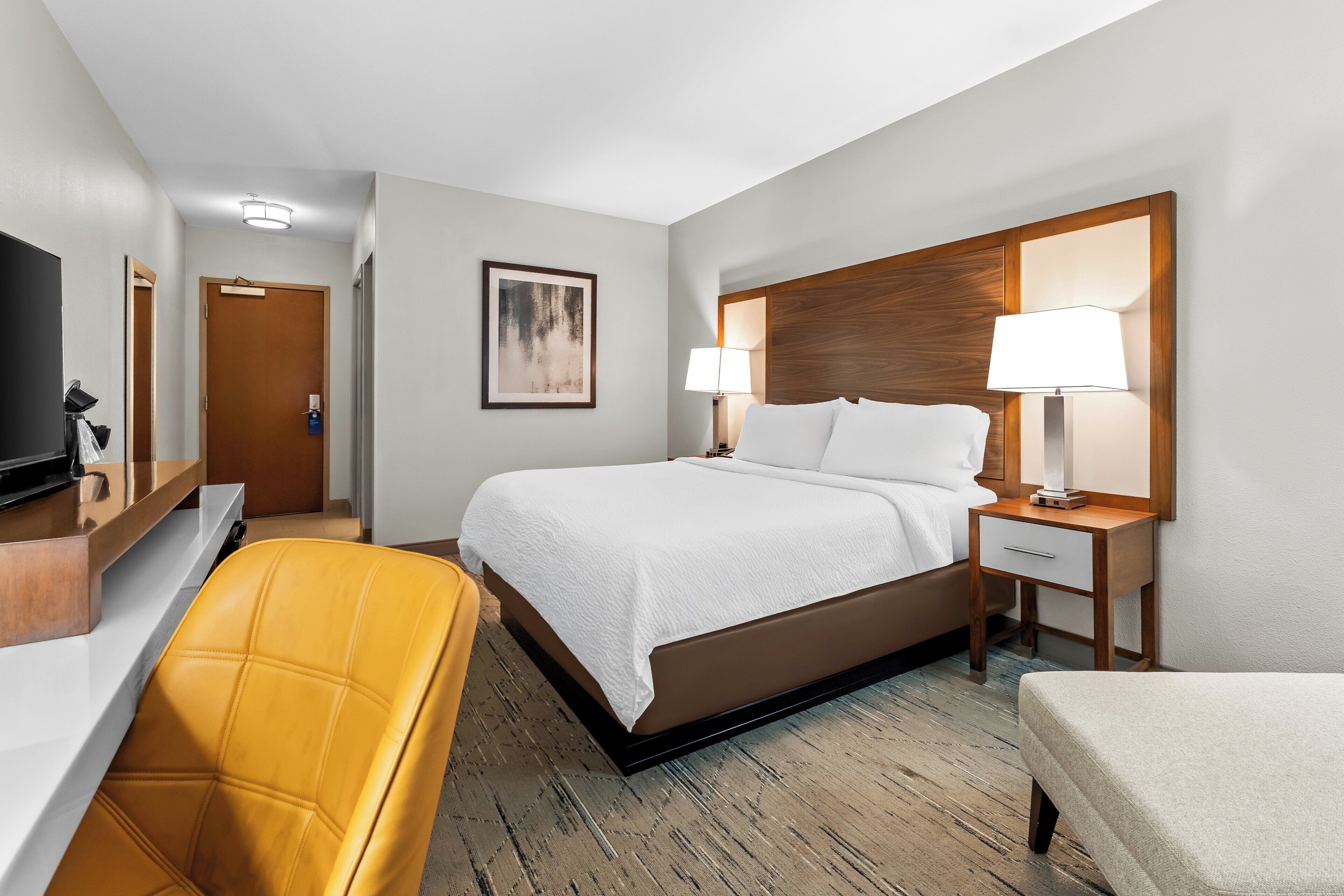 Une chambre d’hôtel comprenant un lit, des tables de chevet, un bureau, une chaise et un téléviseur.