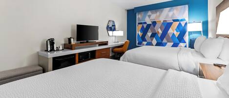 A hotel room with two beds, a desk with a TV, a coffee maker, and a blue geometric wall design.