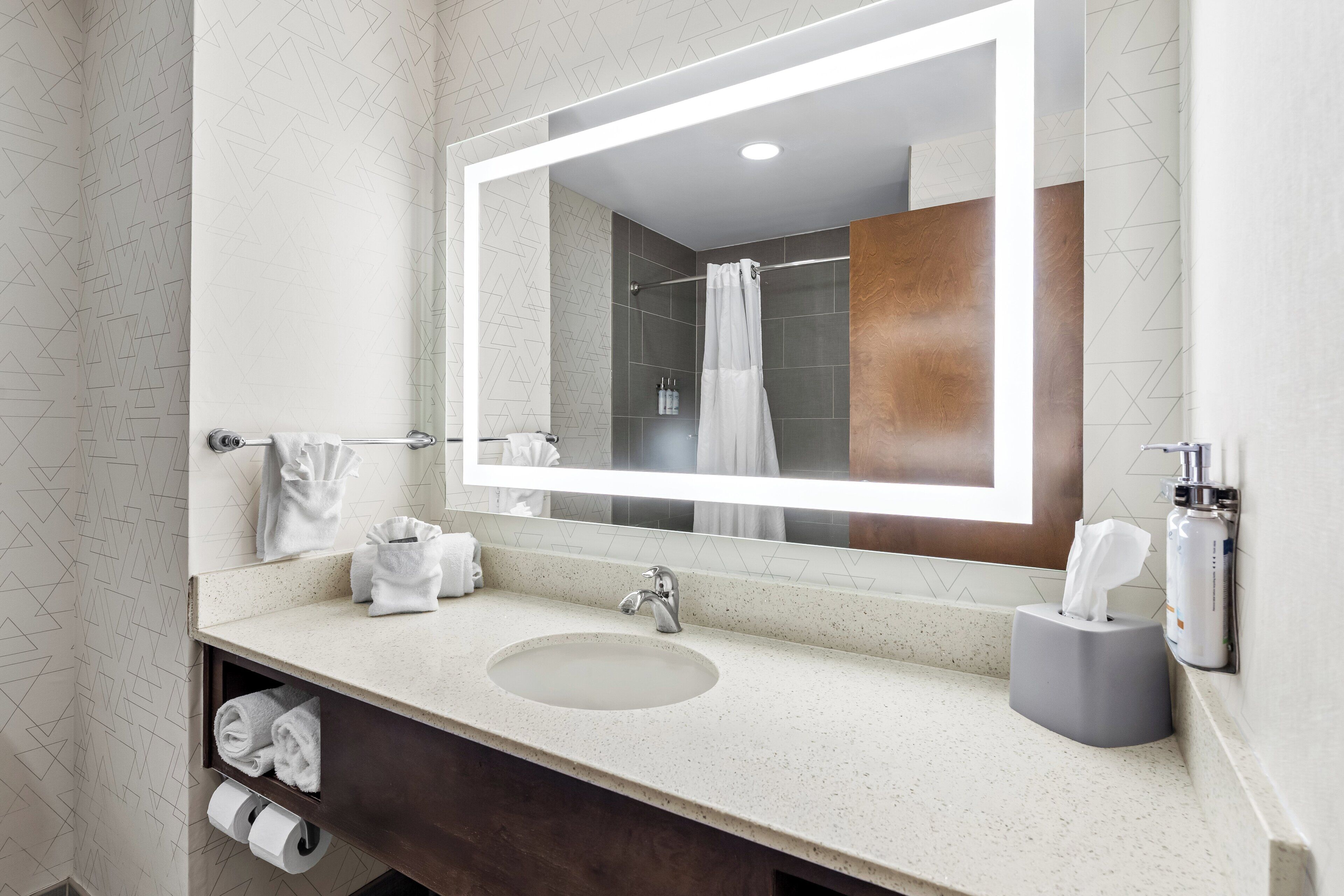 A bathroom with a large mirror, a sink, a towel rack, and a shower area.
