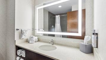 A bathroom with a large mirror, a sink, a towel rack, and a shower area.