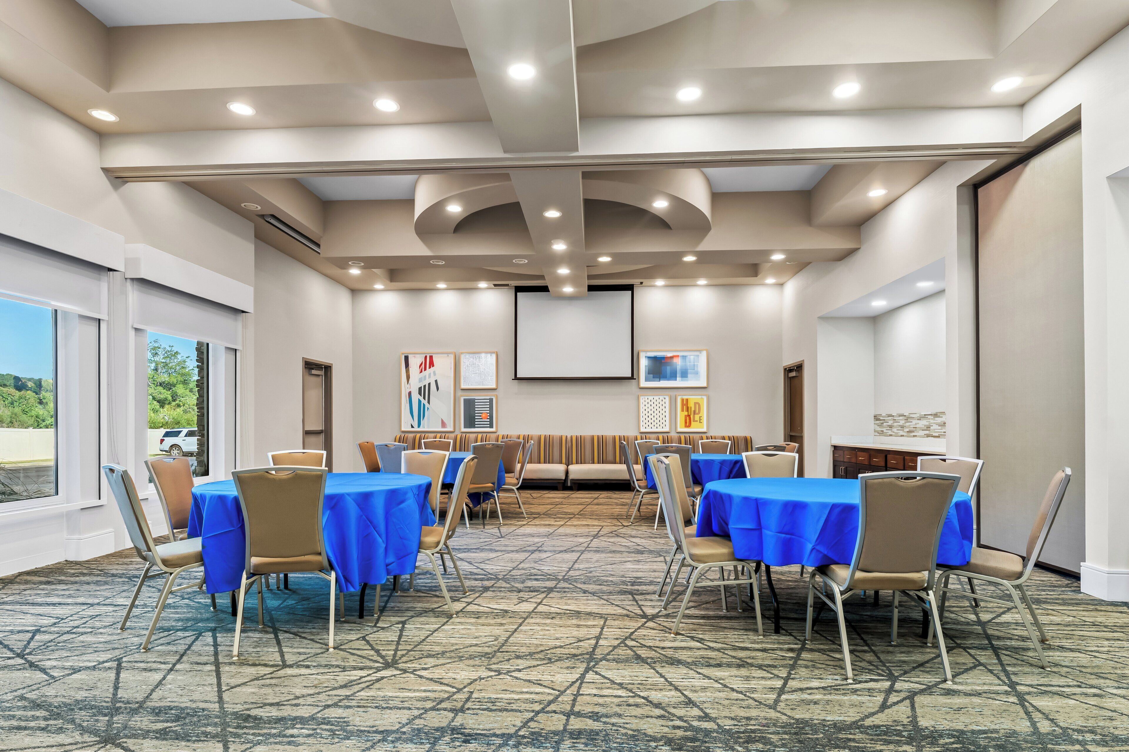 A conference room with round tables, chairs, and a projector screen.