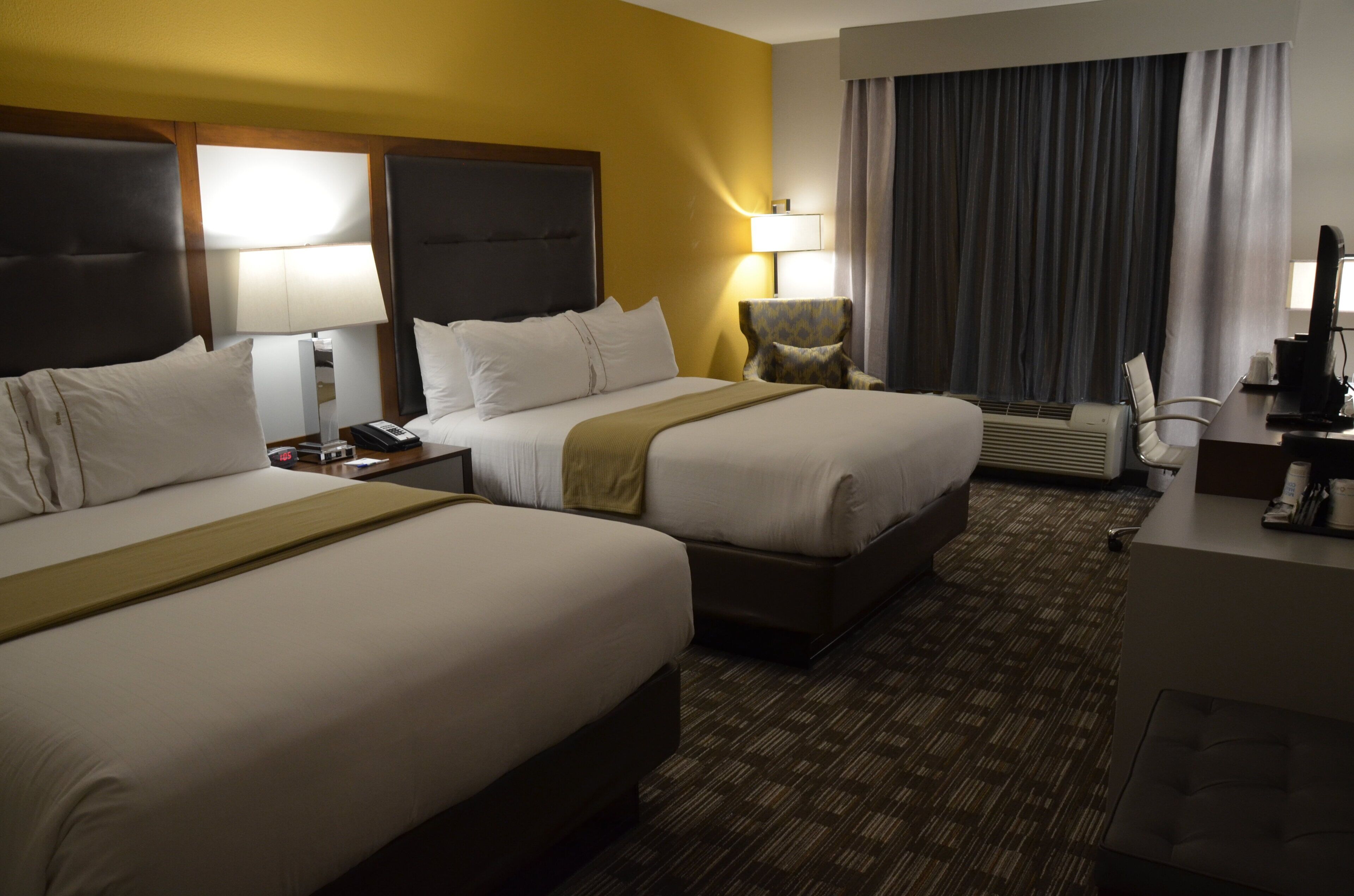 A hotel room with two beds, a desk, a chair, a lamp, and a window with curtains.