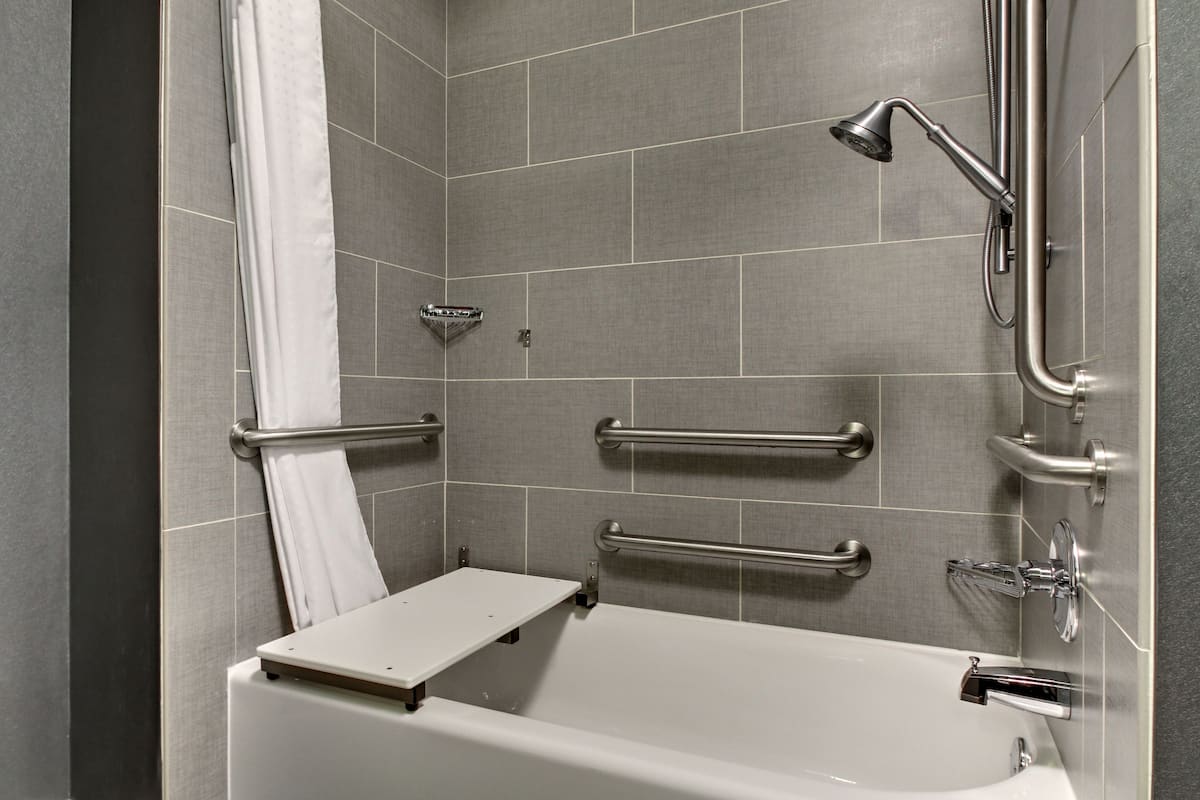 A modern bathroom with a bathtub, grab bars, a showerhead, and a towel rack.