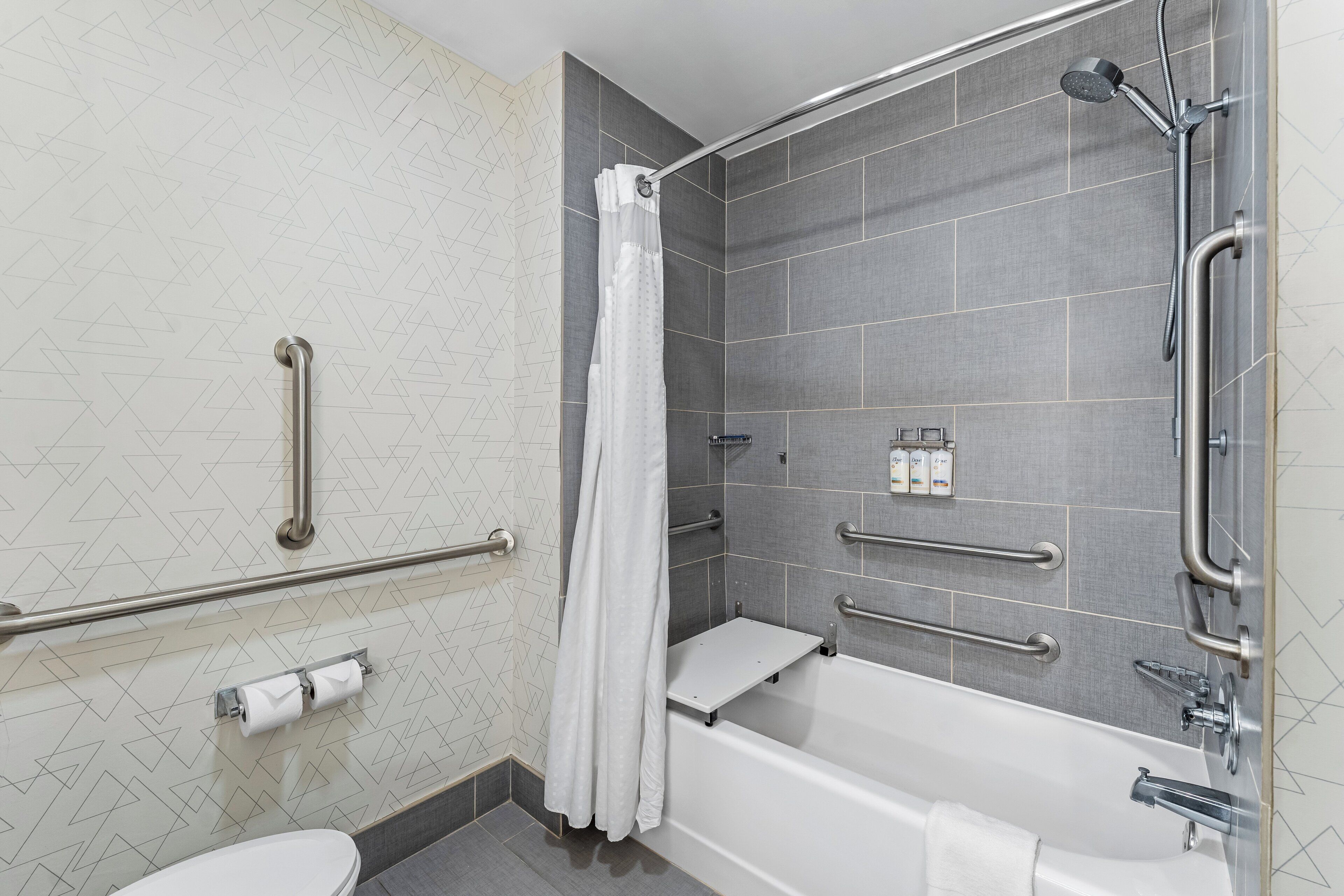 A modern bathroom with a shower, toilet, and grab bars.